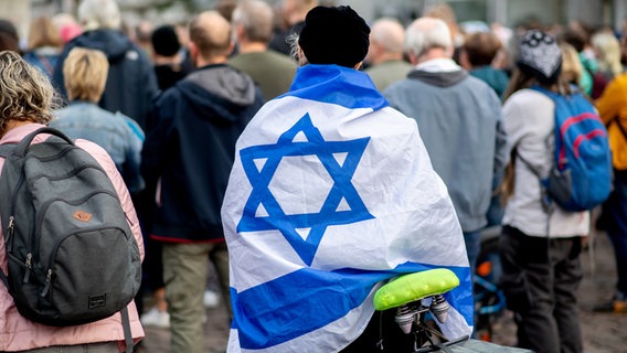 Ein Teilnehmerin einer Kundgebung zur Solidarität mit Israel steht auf dem Julius-Mosen-Platz im Stadtzentrum von Oldenburg, auf ihrem Rücken eine Israel-Fahne. © picture alliance / Hauke-Christian Dittrich 