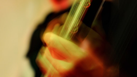 Eine Hand hält den Hals einer Gitarre. Das Bild ist farblich übersteuert und verschwommen. © Guntier / photocase.de 
