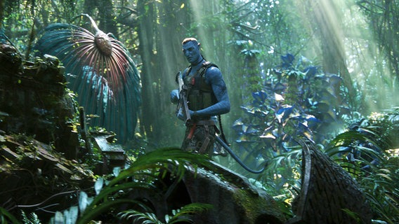 Ein Navi mit Gewehr in der Flora von Pandora - Filmszene aus "Avatar 2 - The Way of Water" von James Cameron © Courtesy of 20th Century Studios 
