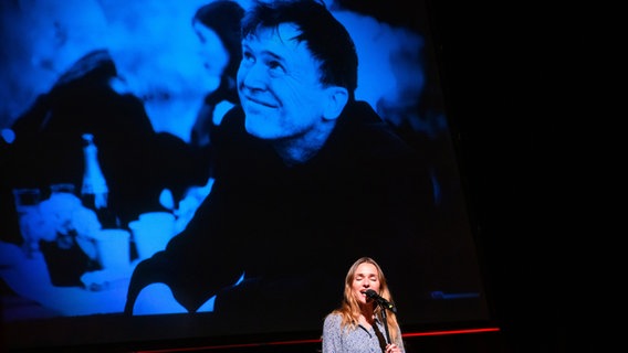Schauspielerin Josephin Busch singt bei einer öffentlichen Gedenkfeier im St. Pauli Theater in Hamburg vor einem Foto des verstorbenen Schauspielers Uwe Bohm. © dpa Foto: Jonas Walzberg