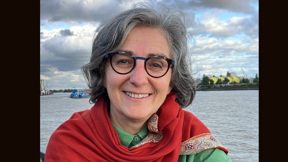 Regisseurin Isabel Herguera mit Brille und rotem Tuch vor der Kulisses der Elbe und des Hafens Hamburg Regisseurin Isabel Herguera mit Brille und rotem Tuch vor der Kulisses der Elbe und des Hafens Hamburg © Fabian&Fred