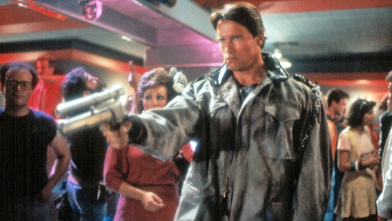 Arnold Schwarzenegger mit einer Waffe in "Terminator" von 1984 von James Cameron © Orion Pictures Corporation/Courtesy Everett Collection | 