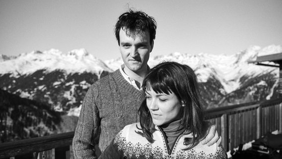 Jan Bülow (l) steht hinter Olivia Roos und schaut in die Kamera, im Hintergrund verschneite Berge © Neue Visionen Filmverleih 