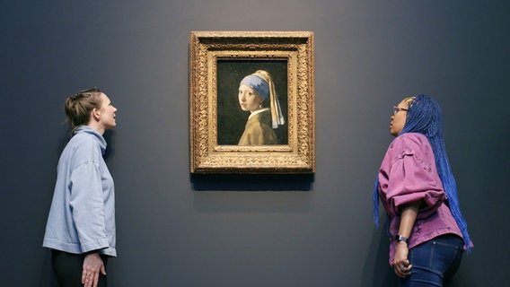 Zwei Mitarbeiterinnen beobachten an einer Wand, ob ein Vermeer-Gemälde richtig gehängt ist - bei der Jahrhundertausstellung "Vermeer" im Rijksmuseum Amsterdam - Filmstill © Neue Visionen 