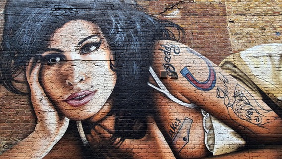 Das Graffity einer Frau mit schwarzen langen Haaren auf einer Ziegelwand © picture alliance Foto: Cover Images | Cover Images