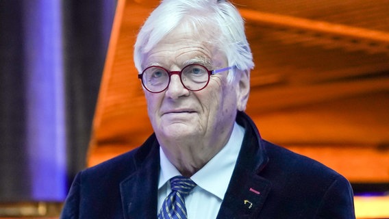 Älterer Mann mit weißen Haaren, Brille und blauem Anzug vor rotem Hintergrund. Es ist Justus Frantz, Gründer des SHMF. © imago/Funke Foto Services 