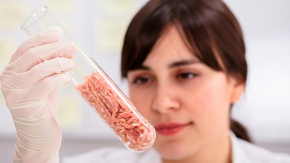Eine Frau betrachtet ein Reagenzglas, in dem Fleisch ist. © mauritius images / Alamy Stock Photos / Andriy Popov 