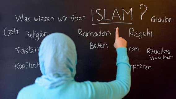 Eine muslimische Schülerin vor einer Tafel mit Begriffen aus dem Islam im Islamunterricht. © imago 
