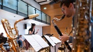 Im Vordergrund ein junger Mann mit einem Saxophon, im Hintergrund dirigiert eine Frau. © picture alliance/dpa | Sebastian Kahnert 