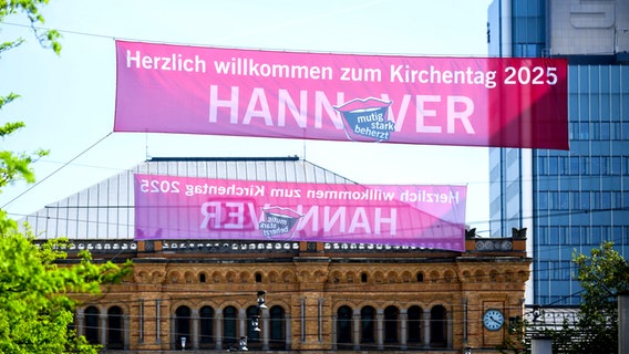 Ein rosa Plakat weist vor dem Hauptbahnhof Hannover auf den Deutscher Evangelischer Kirchentag 2025 hin - darauf steht: Herzlich willkommen zum Kirchentag 2025 Hannover © Julian Stratenschulte/dpa +++ dpa-Bildfunk Foto: Julian Stratenschulte