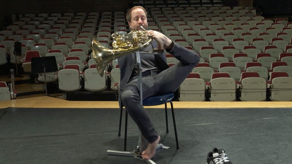 Hornist Felix Kieser sitzt auf einem Stuhl und bedient das Horn mit seinem Fuß. Er hat keine Arme. © NDR 