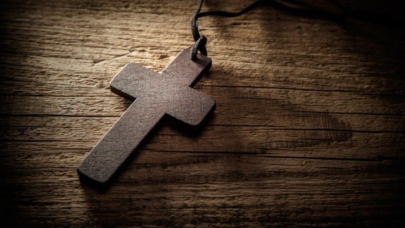 Kreuz am Band liegt auf einem Holztisch © fotolia Foto: merydolla