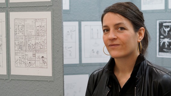 Eine Frau mit Pferdeschwanz vor einer Wand mit Comiczeichnungen © NDR Foto: Mathias Heller