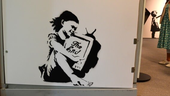 "The End" - ein Mädchen sitzt in einer Ecke mit einem Monitor und der Aufschrift - "The End": Bild einer Replik von Kunst des Graffiti-Künstlers Banksy in der Hamburger Ausstellung "The Mystery of Banksy - A Genius Mind" © NDR Foto: Patricia Batlle