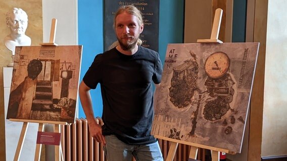 Der Künstler Christian Bröhenhorst steht neben zwei seiner Collagen zum Thema Long-Covid. © NDR Foto: Frederik Schulz-Greve
