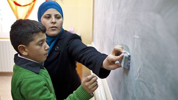 Ein Schüler und eine Lehrerin stehen vor der Tafel © imago 