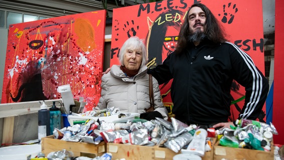 Der Künstler Jonathan Meese steht mit seiner Mutter Brigitte Meese vor zwei seiner Bilder, die in rot gehalten sind. © picture alliance/dpa | Bernd von Jutrczenka Foto: Bernd von Jutrczenka