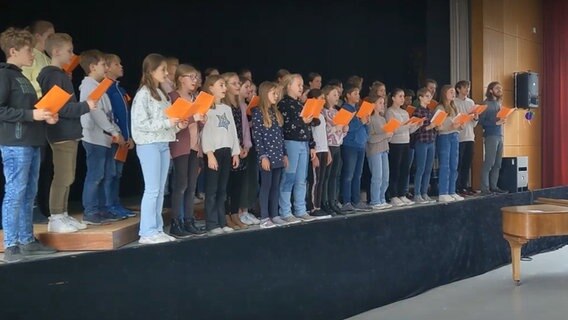 Etwa dreißig Kinder stehen zusammen auf einer Bühne und singen aus Gesangsheften © NDR 