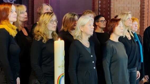 Etwa zehn dunkel gekleidete Frauen stehen in einer Kirche bei einer Kerze und singen © NDR 