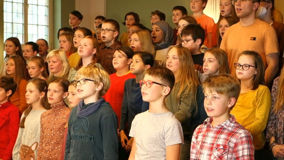 Etwa dreißig Kinder und Jugendliche stehen in fünf Reihen und singen. © NDR 