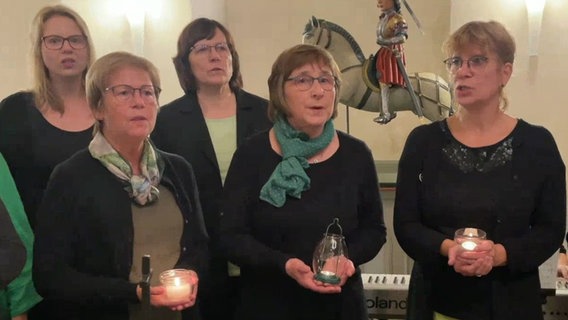Fünf in Grüntönen gekleidete Frauen stehen zusammen und singen, einige halten Windlichter mit Kerzen © NDR 