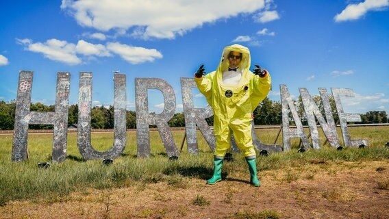 Porky von der Band Deichkind in einem Ganzkörper-Schutzanzug vor einem Hurricane-Schriftzug.  Foto: Benjamin Hüllenkremer