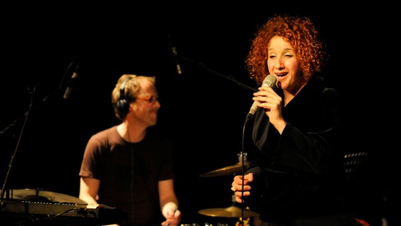 Eine Frau singt in ein Mikrofon. Im Hintergrund spielt ein Mann Schlagzeug. © Sven Thielmann Foto: Sven Thielmann