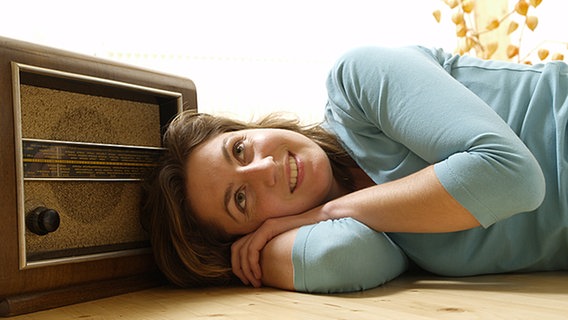 Junge Frau liegt auf dem Boden neben einem alten Radiogerät und hört zufrieden zu. © KPA/Thomas Foto: KPA/Thomas