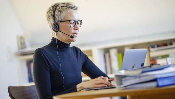 Eine Frau sitzt zu Hause am Schreibtisch. Sie trägt ein Headset und spricht. © picture alliance / photothek | Thomas Trutschel/photothek Foto: Thomas Trutschel