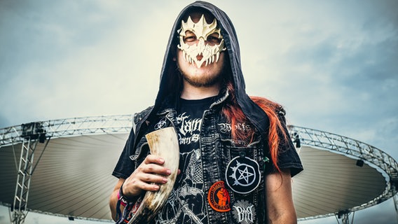 Ein Mann mit Kapuze, einer Knochenmaske vor dem Gesicht und einem Trinkhorn in der Hand © NDR Foto: Benjamin Hüllenkremer