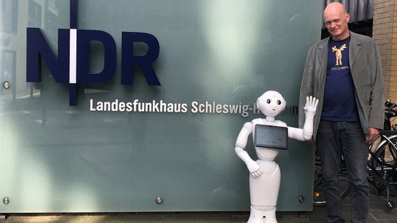 Roboter Pepper und Programmierer Thomas Sievers stehen vor dem Eingang des Landesfunkhauses Schleswig-Holstein. © Thomas Sievers Foto: Thomas Sievers