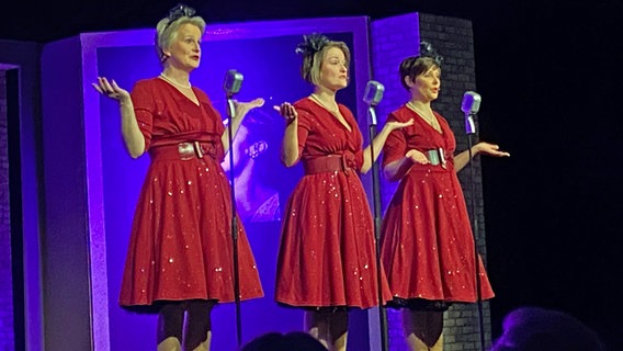 Drei Schauspielerinnen in roten Kleidern stehen nebeneinander auf der Bühne. © NDR Foto: Jan Graf