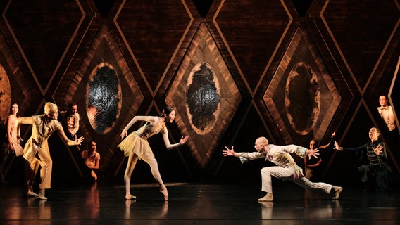 Verschiedene Darsteller des Balletts "Petruschka / Der Feuervogel" tanzen in zwei Gruppen, die sich gegenüberstehen, auf einer Bühne. © Admill Kuyler 