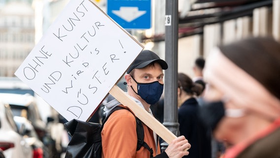 Ein Schauspieler vom Residenztheater steht mit einem Schild mit der Aufschrift "Ohne Kunst und Kultur wirds düster!" in einer Menschenkette. © dpa Foto: Matthias Balk