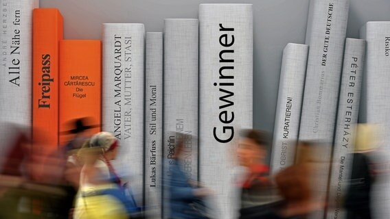 Besucher der Leipziger Buchmesse gehen an einer mit Buchrücken bedruckten Wand vorüber. © dpa Foto: Hendrik Schmidt