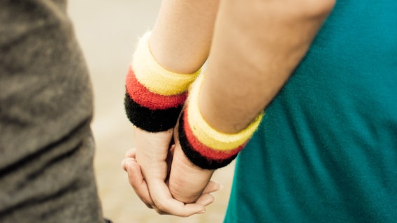 Ein Paar hält sich an den Händen - beide tragen Deutschland-Armbänder. © Photocase/ Andrey-fo Foto: Andrey-fo
