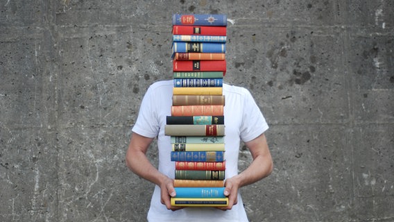 Ein Mann hält einen Stapel Bücher. © NDR 