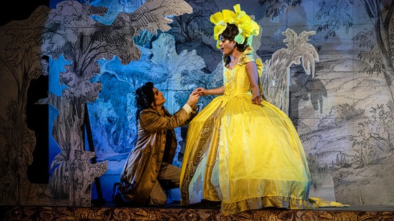 Ein Mann kniet auf einer Bühne vor einem anderen Mann, der ein gelbes Kleid trägt. Beide fassen sich an den Händen. © Alciro Theodoro da Silva 