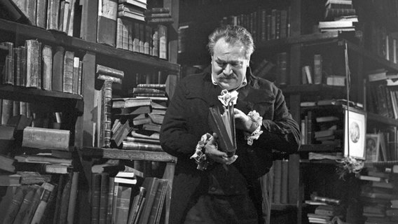 Ein Mann steht vor einem Bücherregal und blättert in einem Buch © picture alliance/United Archives | Siegfried Pilz 