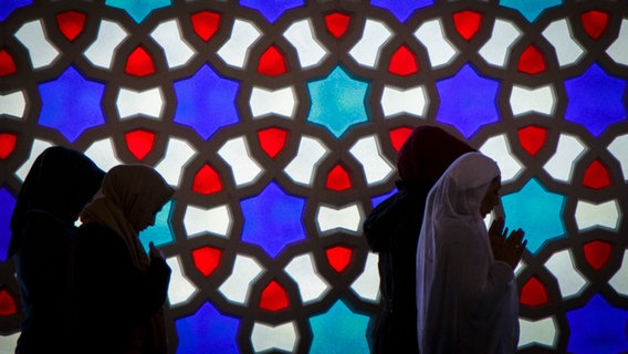 Frauen stehen vor einem bunten Fenster in einer Moschee und beten. © picture alliance / photothek Foto: Thomas Trutschel
