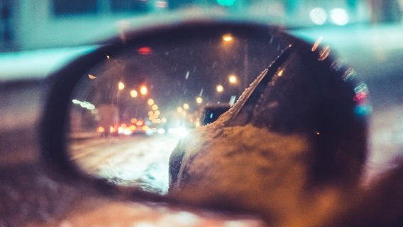 Im Rückspiegel eines Autos sind eine verschneite Straße im Dunkeln und Scheinwerfer zu sehen. © Picjumbo 