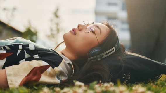 Junge asiatische Frau entspannt sich mit Kopfhörern auf dem Rasen © Photocase Foto: Standret