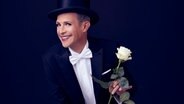 Tim Fischer, in Konzertgarderobe, lächelt mit einer weißen Rose in der Hand in die Kamera. © Benno Kraehahn Foto: Benno Kraehahn