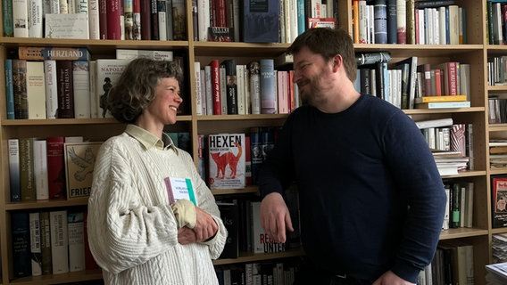 Lisa Kreißler und Alexander Solloch stehen sich zugewand an einer Bücherwand gegenüber. © NDR Foto: Julia Beyer