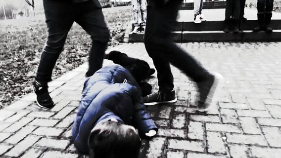 Ein am Boden liegender Junge wird von zwei Jugendlichen getreten. © NDR 