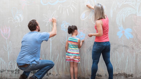 Eine Familie bemalt eine Betonwand mit bunter Kreide © picture alliance / Westend61 Foto: zerocreatives