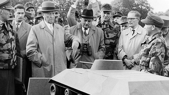 Konrad Adenauer und Franz Josef Strauß umringt von Bundeswehrpersonal und Fotografen vor einem Panzer-Modell. Konrad Adenauer und Franz Josef Strauß umringt von Bundeswehrpersonal und Fotografen vor einem Panzer-Modell. © dpa