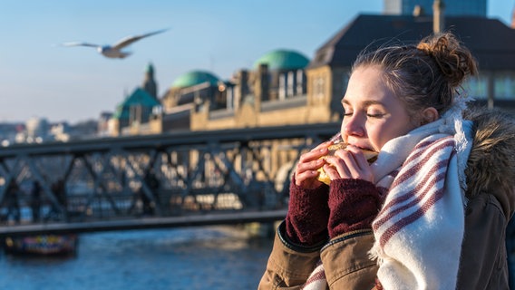 Eine Frau isst ein Brötchen im Hamburger Hafen. © Getty Images | iStockphoto Foto: Jens Rother