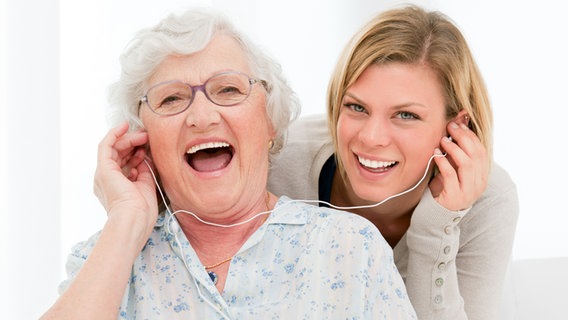 Eine junge und eine alte Frau haben jeweils einen Knopf eines Kopfhörers im Ohr und lachen. © PantherMedia Foto: ridofranz