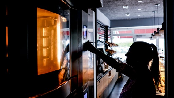 Eine Mitarbeiterin einer Bäckerei in Hamburg öffnet im abgedunkelten Geschäftsraum den Backofen. © Axel Heimken/dpa 